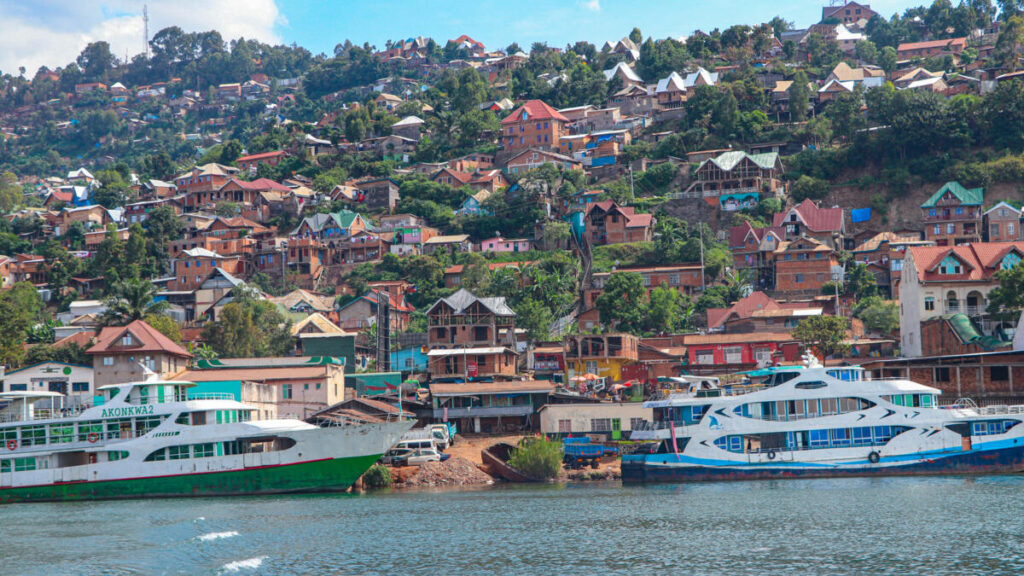 Hilly waterfront town with colorful houses on a steep slope and two large white passenger ferries docked along the shore.