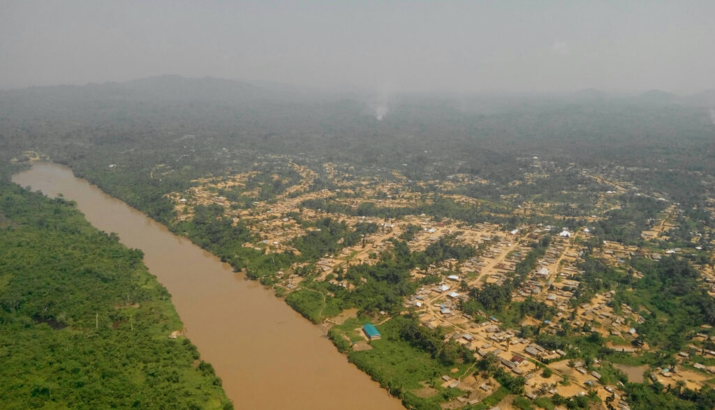 Aerial view of a muddy river winding through a green valley with a dense rural village of tan-roofed houses on both banks.